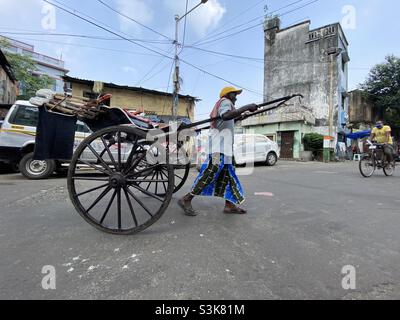 A Rickshaw puller manually driving the rickshaw in the street of Kolkata Stock Photo