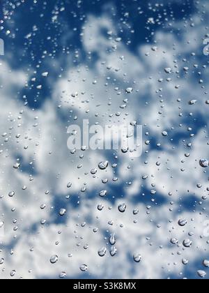 Water droplets on a window with blue sky and clouds behind Stock Photo