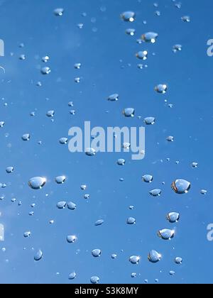 Water droplets on a window with blue sky behind Stock Photo