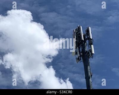 A cell tower set against an early springtime blue sky and billowing clouds. Stock Photo