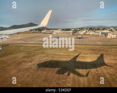 The shadow of a Boeing 737-800 landing at Townsville Airport, Queensland, Australia showing the wing tip and military aircraft in the background.
