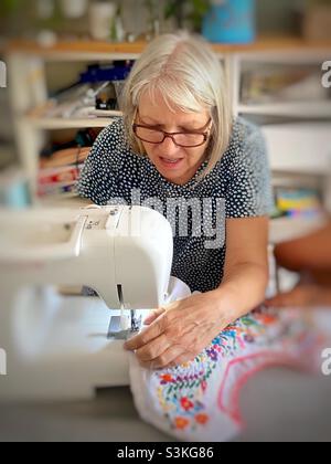 A woman sewing a colorful blouse on a sewing machine Stock Photo