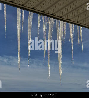 Icicles hanging from a balcony, highlighted against a blue sky. Stock Photo