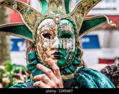 A reveller conceals their face behind an elaborate Venetian mask in green and gold Stock Photo