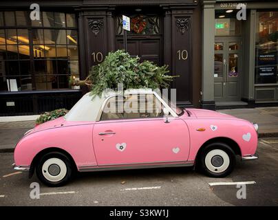 A pink car is seen with a Christmas tree tied to the roof in central London. Stock Photo
