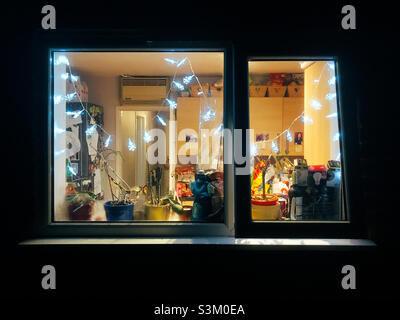 Kitchen window adorned with Christmas lights seen from the outside at night. Stock Photo
