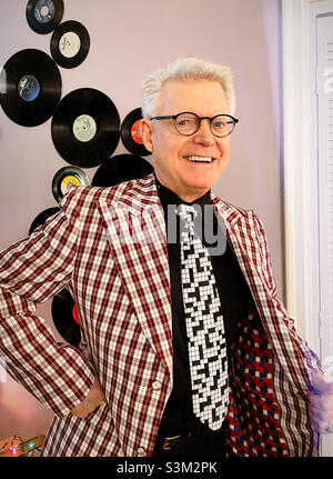 Senior man shows off his multi colored lining of a plaid jacket in front of a display of retro vinyl records, 2021, United States Stock Photo