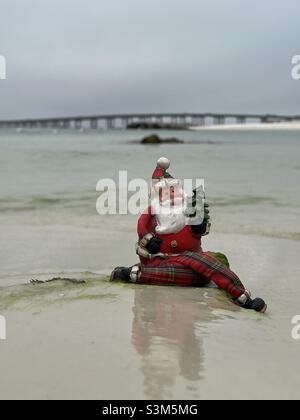 Santa Claus figurine setting on the beach with blur background of Destin Florida bridge Stock Photo