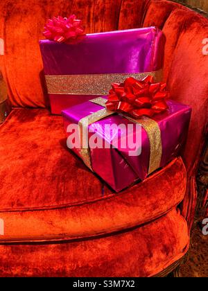 Presents or gifts wrapped in colorful paper with glitter ribbons and bows on velvet sofa for holiday gift giving Stock Photo