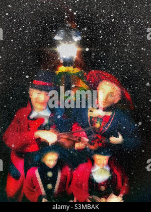 A thrift store find, this family of Victorian era carolers in holiday dress of red and green sing Christmas carols under lamplight as the snow is falling. Stock Photo