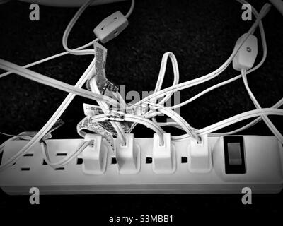 A power strip under a living room table has multiple plugs in its’ sockets during the Christmas season to accommodate all the lighted decorations. Stock Photo