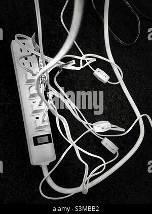 A power strip under a living room table has multiple plugs in its’ sockets during the Christmas season to accommodate all the lighted decorations. Stock Photo