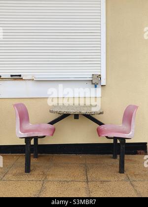 Faded seats at a table at a seaside café, closed for the winter Stock Photo