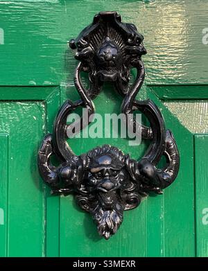 A door knocker with lion masks on a bright green front door Stock Photo