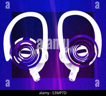 Newest pair of Apple AirPods Pro, with ear hook accessories attached. Colored frame, background and rippled effects (representing sound) have been added digitally for artistic effect. Stock Photo
