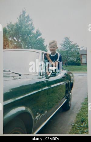 Vintage American 1960’s young boy leaning out of 1967 Ford Mustang fastback Stock Photo