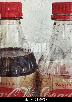 A stylized, with grunge effects, still life of two bottles of Vanilla Coke. One bottle is full while the other has the better part already consumed. Stock Photo