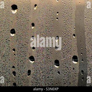 Droplets of water running down a window pane obscured with condensation Stock Photo