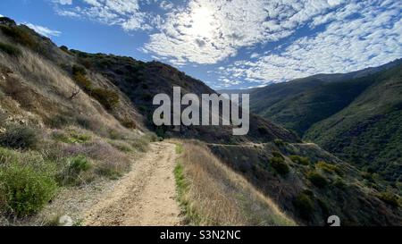 Hiking trail leading down to a winding section through Santa Monica Mountains at Point Mugu State Park, California. Lots of small clouds in sky Stock Photo