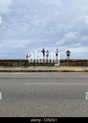 Man spending time together in Malecón, Havana, Cuba. One man fishing, four men watching. Leisure and relax. Stock Photo