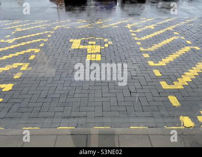 The wet paving outside a Worcester supermarket marked out in yellow, the paving blocks painted to outline disabled parking spaces