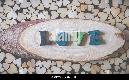 The word LOVE spelt out in wooden letter on a wood with live edge, surrounded by wooden hearts Stock Photo