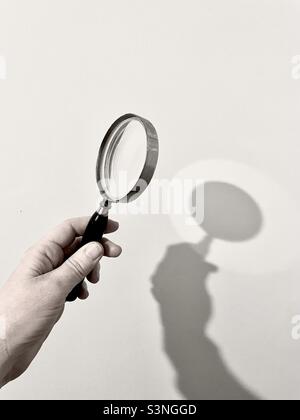 Hand holding a magnifying glass making a shadow on wall. Stock Photo