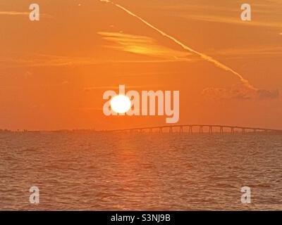 Brilliant orange sky with the huge sun going down over a bridge and coastline in ft Myers beach, Florida, view from a boat on the water, silhouette sunset Stock Photo