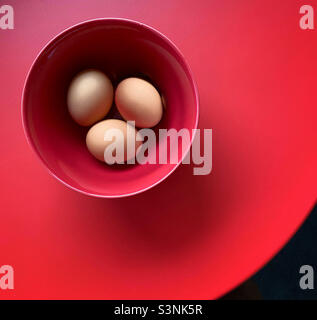 Brown organic eggs in a red bowl on a red table Stock Photo