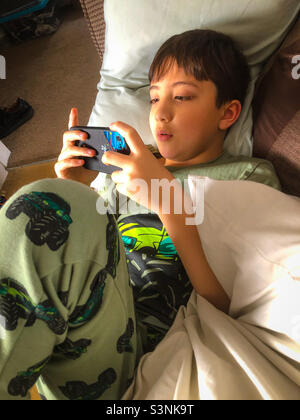 A boy playing a game on a mobile phone while lying on a sofa. Stock Photo