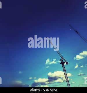 Two construction cranes and white fluffy clouds against a saturated blue sky. Stock Photo
