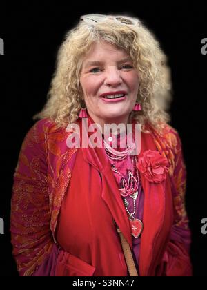Smiling blonde woman dressed in red and pink vibrant clothing at Spitalfields Market London Colourwalk Stock Photo
