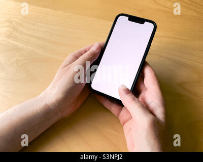 Closeup of female hands holding smartphone with blank white screen as copy space over wooden desk Stock Photo