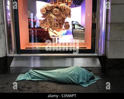 A homeless person sleeps in a blanket in front of a shop window in Pitt Street Mall, Sydney, Australia Stock Photo