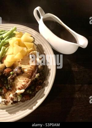 Cottage Pie served with green beans, swede and gravy in a gravy boat Stock Photo