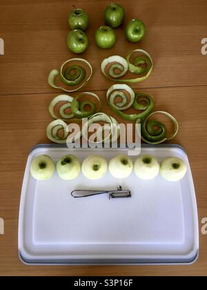 Green apples with peel and tool, on white board and brown wooden table Stock Photo