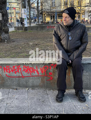 Elderly man sitting on bench & Never Grow Up graffiti - Mitte, Berlin, Germany Stock Photo