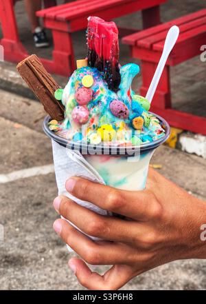 Hand holding a delicious and colourful ice cream cup with a chocolate flake and marshmallows Stock Photo