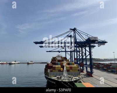 Big container vessel from MSC company in port of Piraeus, Greece under the gantry cranes during cargo operation in spring season with calm sea and blue sky. Stock Photo