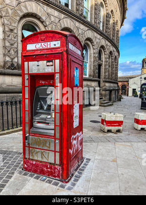 Old fashioned red telephone box as an atm cash machine vandalised in Leeds West Yorkshire Stock Photo