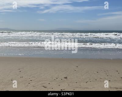 Sun glints off gently breaking Pacific Ocean waves at Ventura Beach, California. Sailboat and islands in distance Stock Photo
