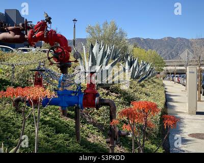 Colorful red and blue pipes surrounded by flowers and vegetarian at the side of a street in La Cañada Flintridge, California, with mountains in background Stock Photo