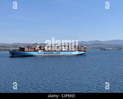 Big loaded Maersk container vessel anchored on the anchorage in front of port of Koper, Slovenia. In background is are visible mountains under blue sky during calm spring weather. Stock Photo