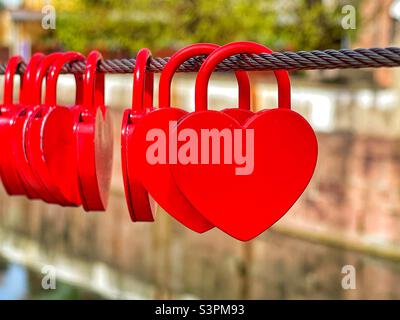Red heart shaped locks on a steel wire cable. No people. Stock Photo