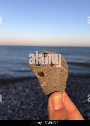 Stone with four holes on being held in hand in evening light by the sea Stock Photo