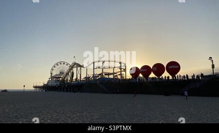 SANTA MONICA, CA, APR 2021: sun setting behind red balloons on the pier, silhouetting roller coaster and Ferris wheel Stock Photo