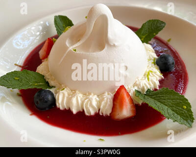 Delicious Pavlova dessert on a white plate close-up.  Pavlova dessert is an airy soft cloud and an amazing taste combination of berries, butter cream and protein dough Stock Photo