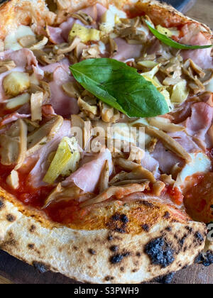 Delicious pizza Capriciosa consisting of tomatoes, Mozzarella cheese, ham, marinated mushrooms, artichoke, basil and butter.  Pizza is made in the oven Stock Photo