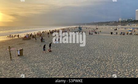 People enjoying the last of the afternoon light on the beach at Santa Monica. Silhouettes and Covid-19 masks make everyone anonymous Stock Photo