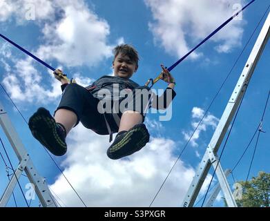 A young boy enjoying bouncing on a bungee frame, beneath a blue sky. Stock Photo
